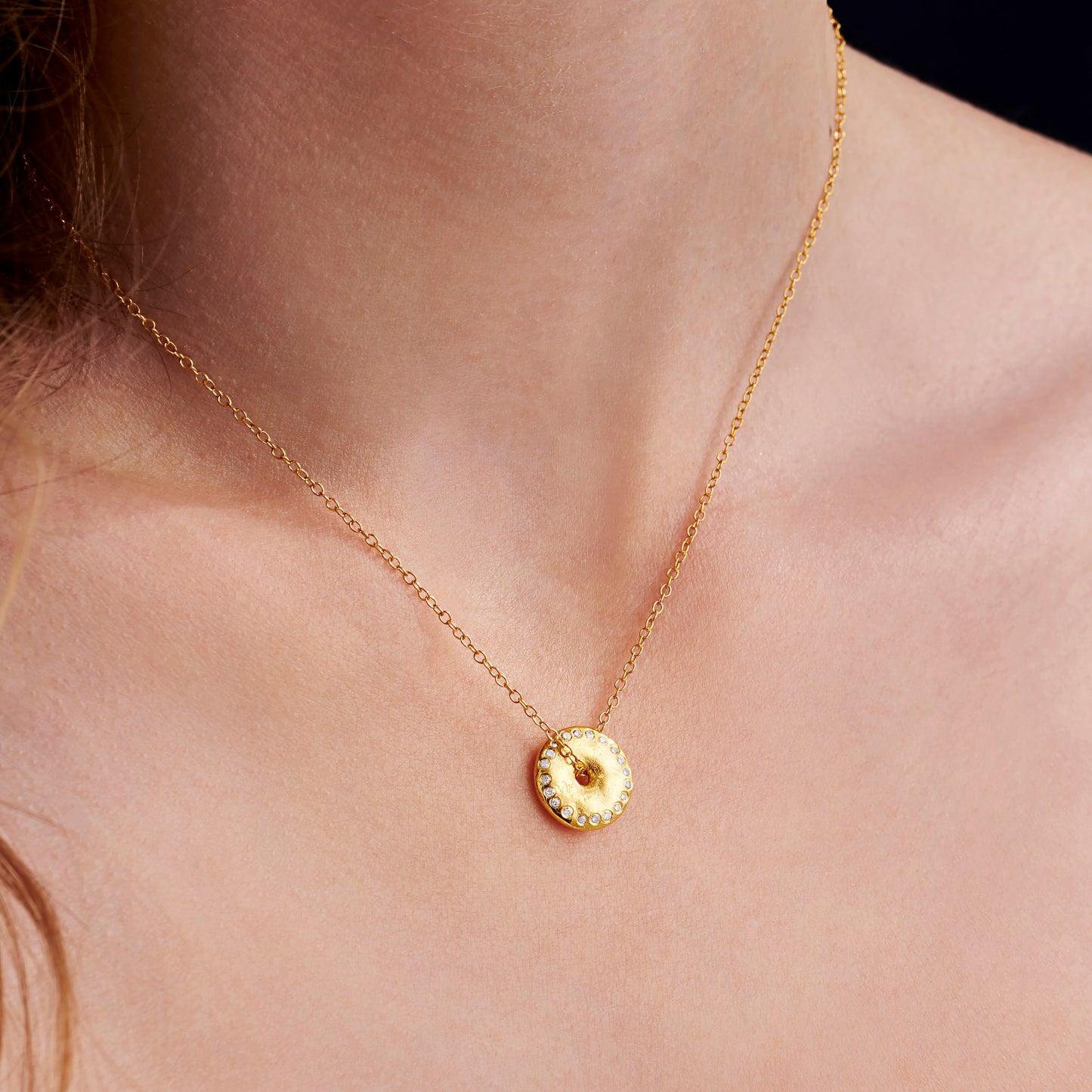 Gold moon phase necklace with a small gold disc pendant with diamonds set around the edge on a person's neck against a neutral background by Claudette Worters