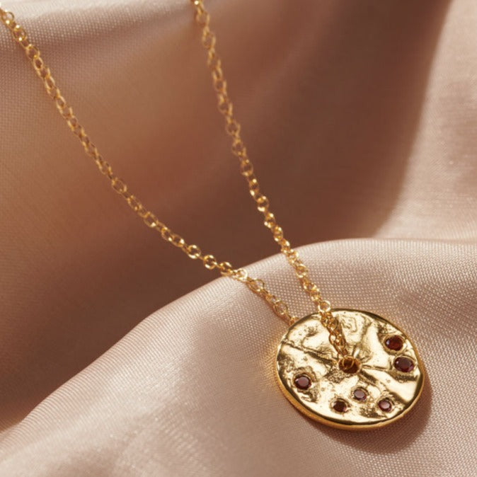 Disc shaped spinner pendant in gold set with dark red garnet stones with a hole in the middle with a fine trace chain running through the centre