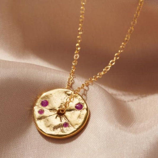 Gold disc pendant with textured surface like an ancient coin.  The pendant is set with faceted rubies.  It has a hole in the centre of the pendant and a dainty trace chain runs through the middle.