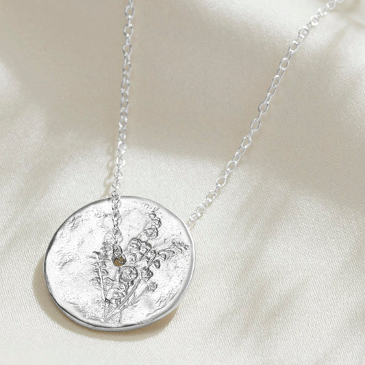Solid silver circle July birth flower pendant with hand engraved Larkspur flower design.  The pendant has a hole in the middle and a delicate sterling silver trace chain is running through the centre of the piece.