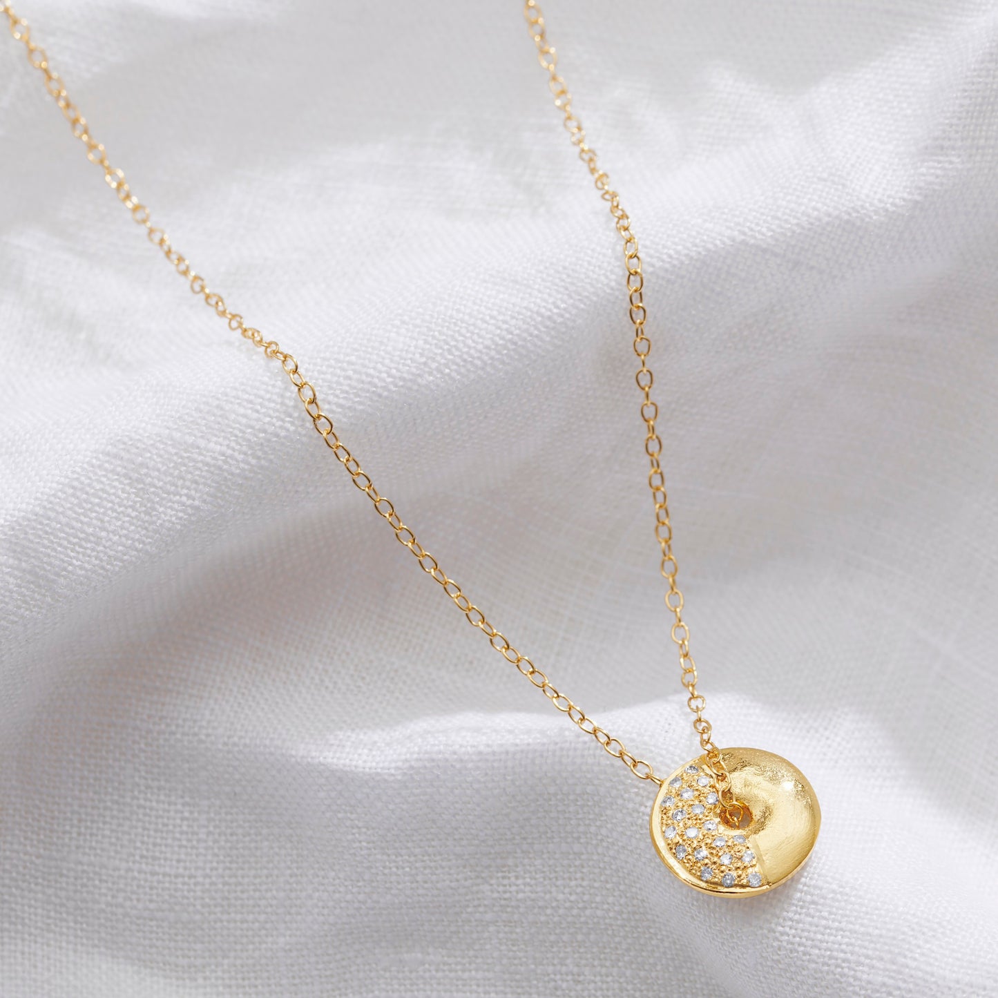Half moon moon necklace by Claudette Worters. A small circular gold disc pendant with a textured moon-like surface set with diamonds on one side to depict the Third Quarter moon phase.