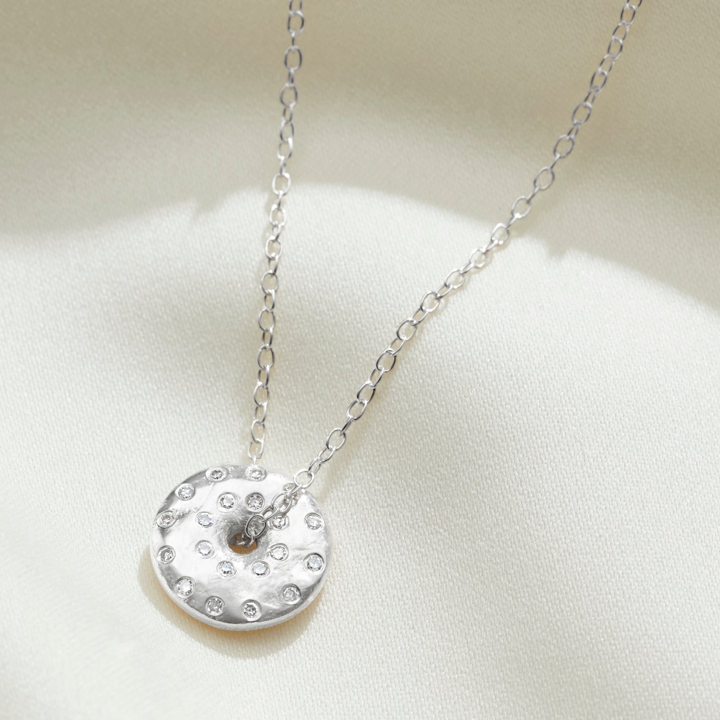 Silver spinning disc pendant set with tiny white diamonds to depict the full moon by Claudette Worters