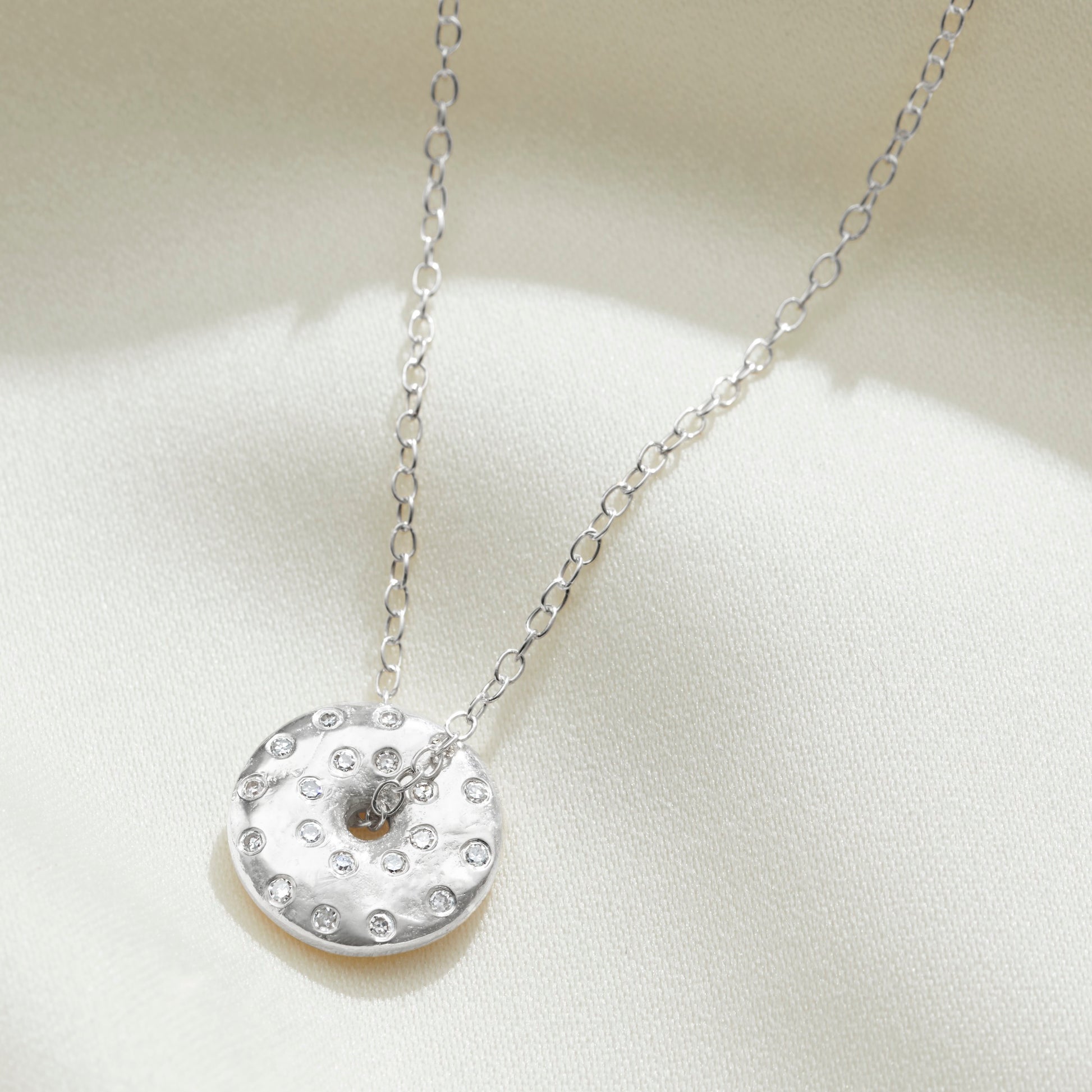 Silver spinning disc pendant set with tiny white diamonds to depict the full moon by Claudette Worters