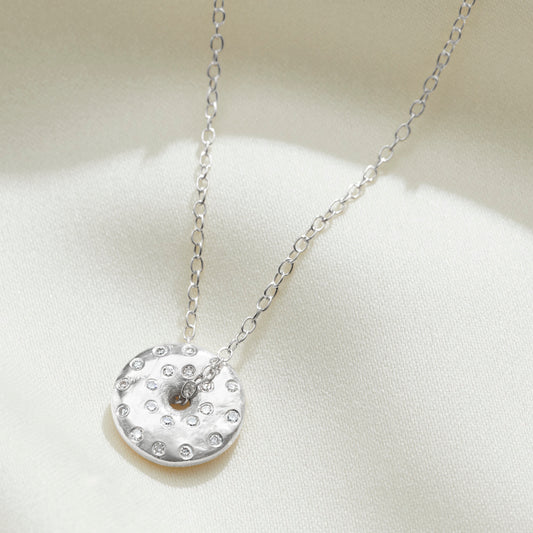 Silver spinning disc pendant set with tiny white diamonds to depict the full moon by Claudette Worters