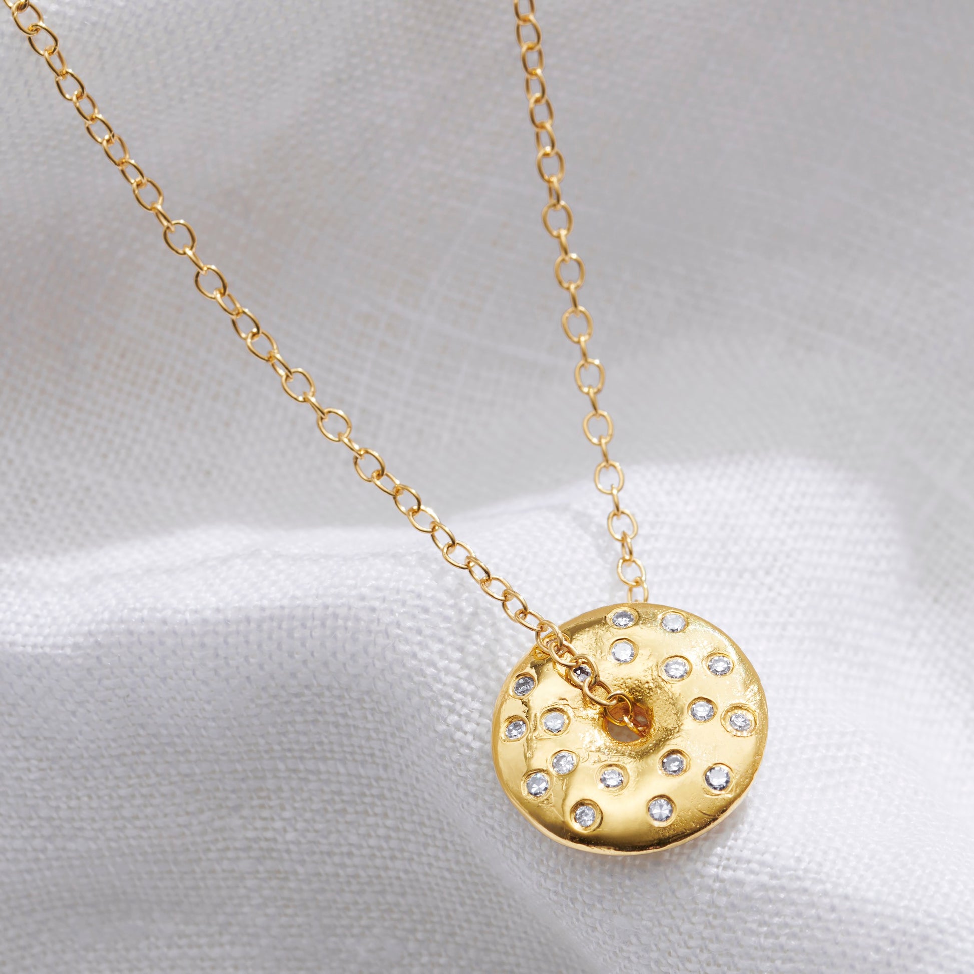 Gold necklace with a circle shaped with a round pendant set with white diamonds with a hole in the middle to represent a full moon on light weight gold trace chain.
