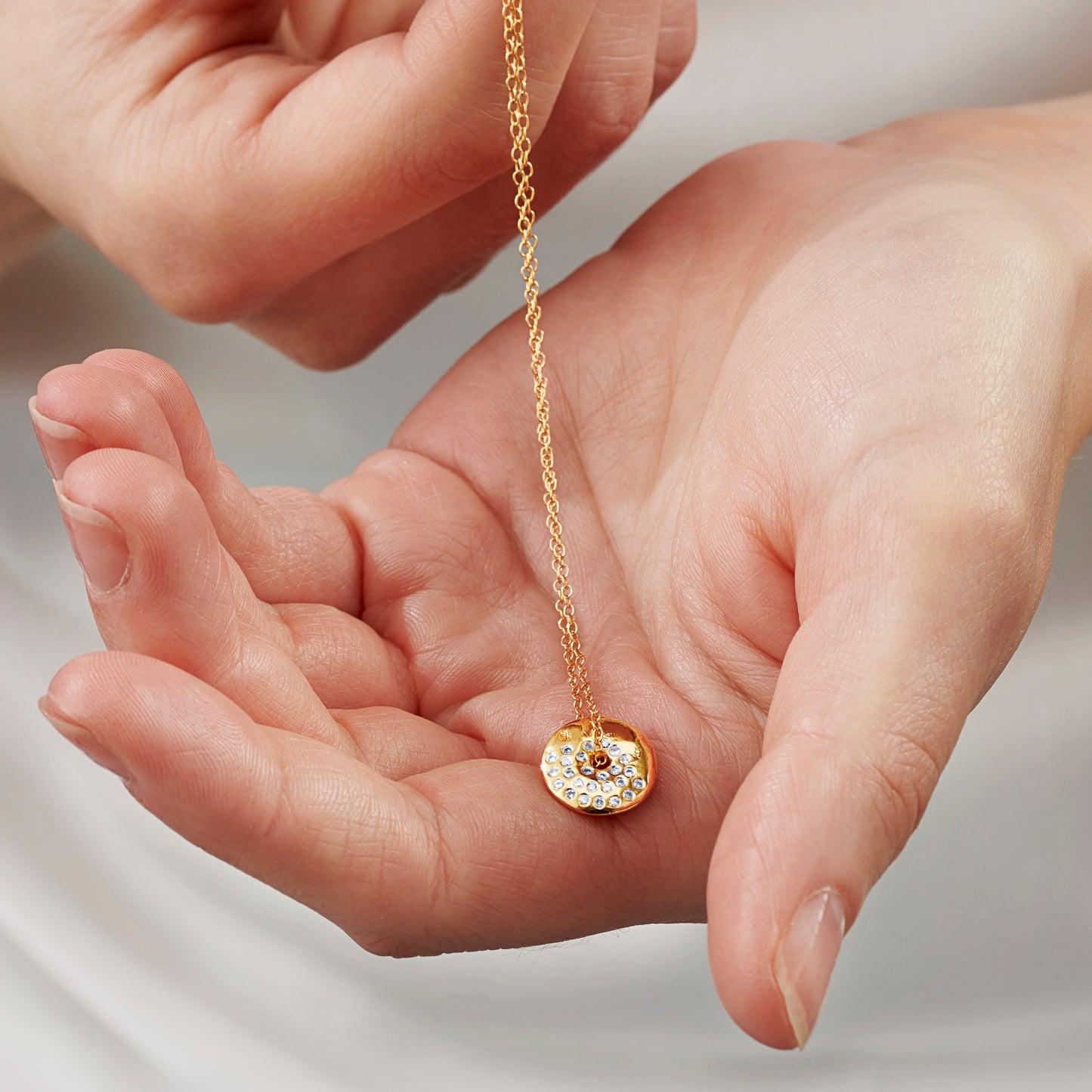 Gold moon phase necklace with a gold disc pendant on a gold chain held in a hand against a neutral background by Claudette Worters