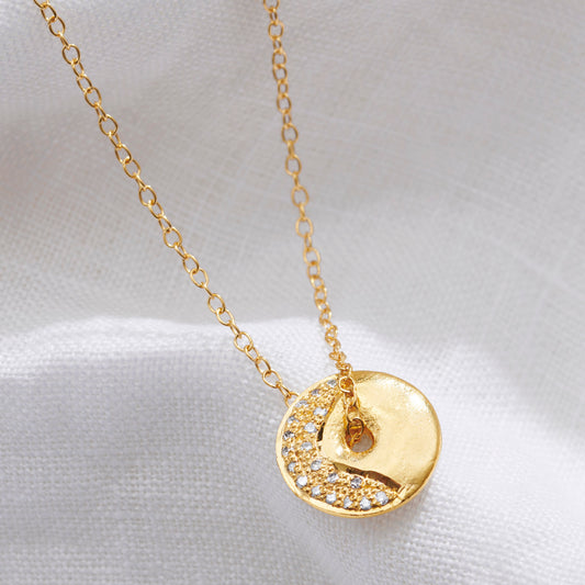 Gold vermeil Waning Crescent moon necklace by Claudette Worters. A small circular gold disc with an organic, crater-like moon texture. A slim arc of tiny diamonds forms the waning crescent. The pendant has a centre hole that lets the disc spin gently on the fine gold chain.