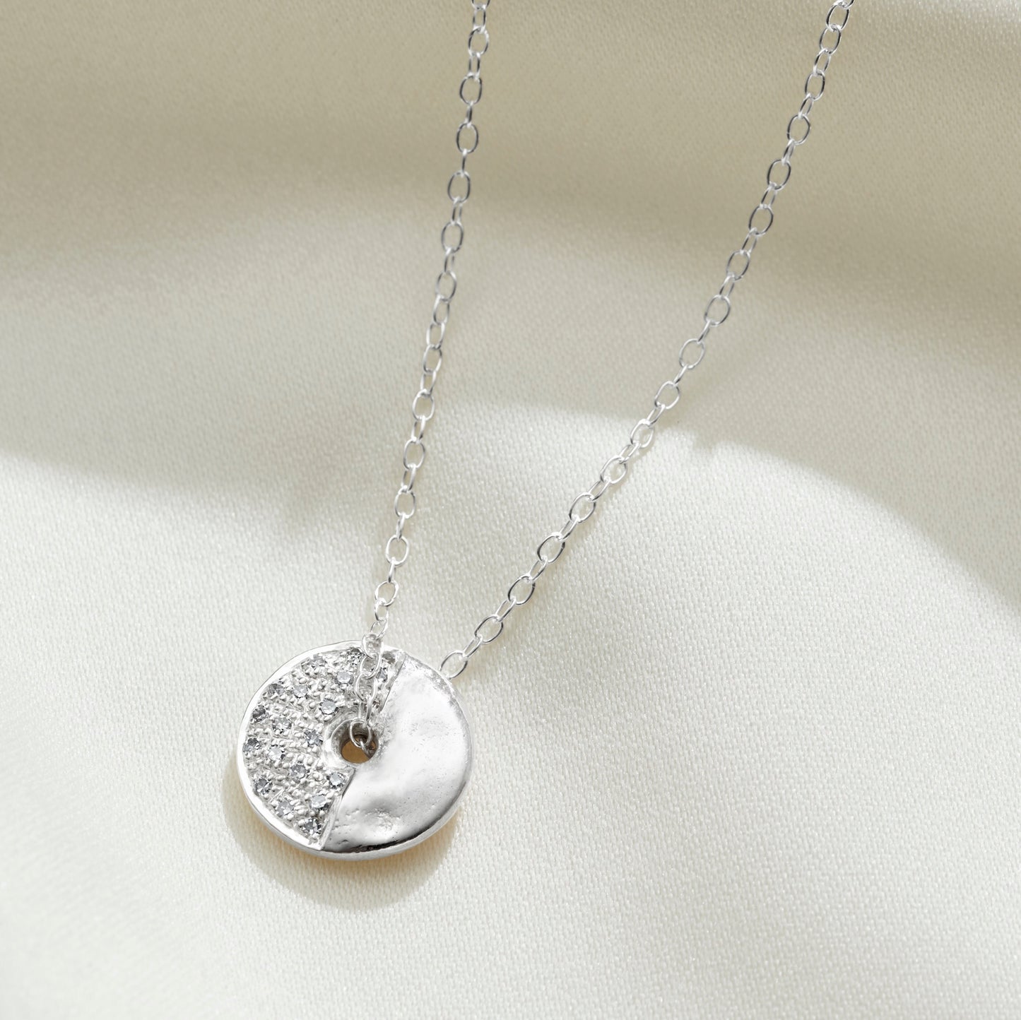 Silver necklace with a round pendant set with diamonds with a chain threading through the centre to represent the third quarter phase of the moon