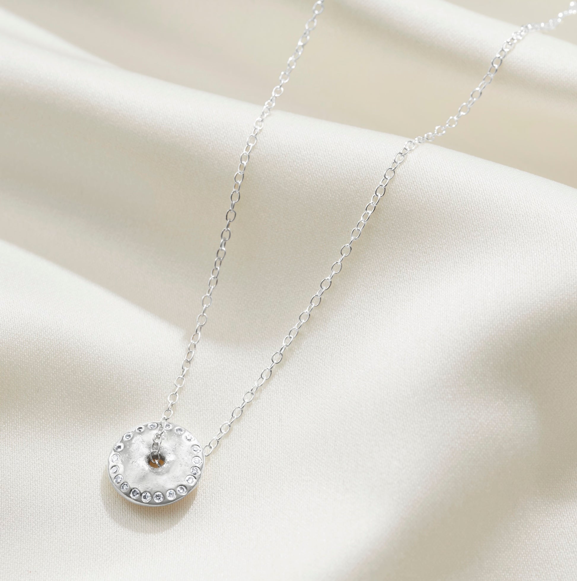 Silver moon phase pendant with a disc pendant set with a ring of white diamonds on a delicate sterling silver trace chain