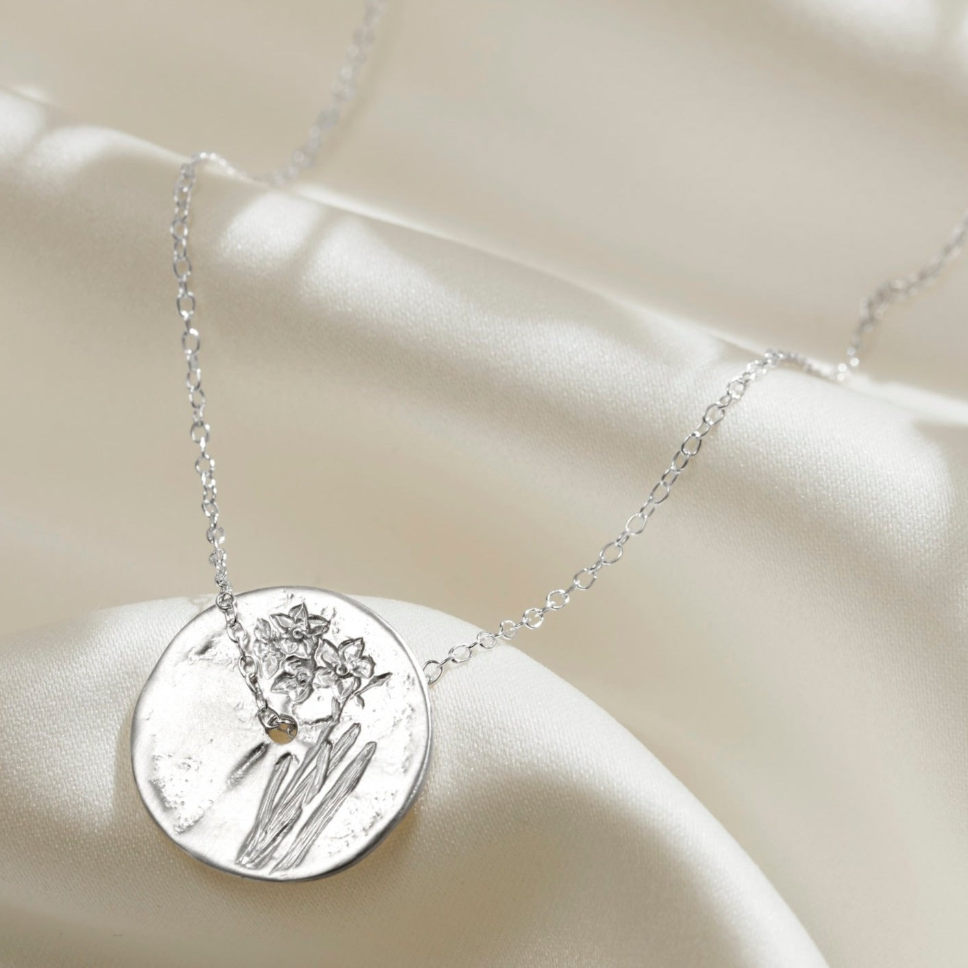 Solid silver medallion style pendant with hand engraved Narcissus birth flower on the front.  The pendant has a hole in the middle with a dainty sterling silver trace chain running through the centre turning it into a spinner pendant necklace.