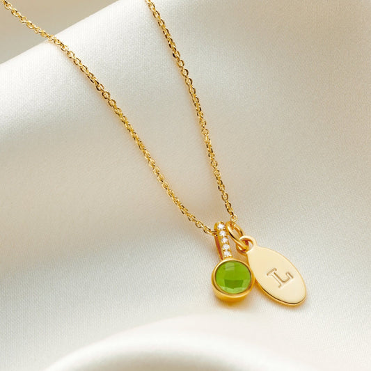 Faceted Peridot birthstone pendant necklace in yellow gold vermeil with tiny white diamonds in the bale on a fine trace chain with a small oval charm personalised with the letter L. 