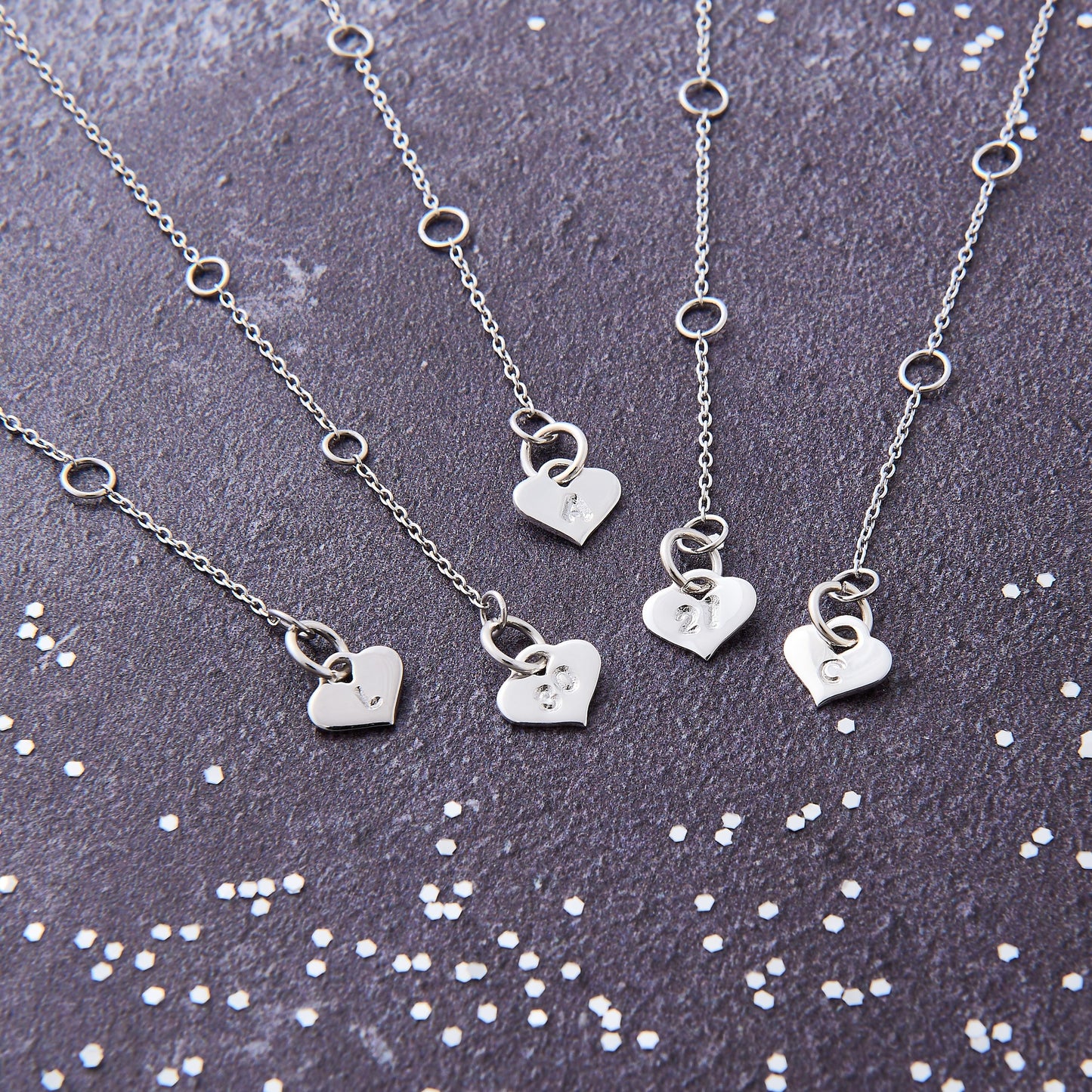 Sterling silver heart charms hand stamped with letters and numbers on the end of a fine trace chain extender chain.