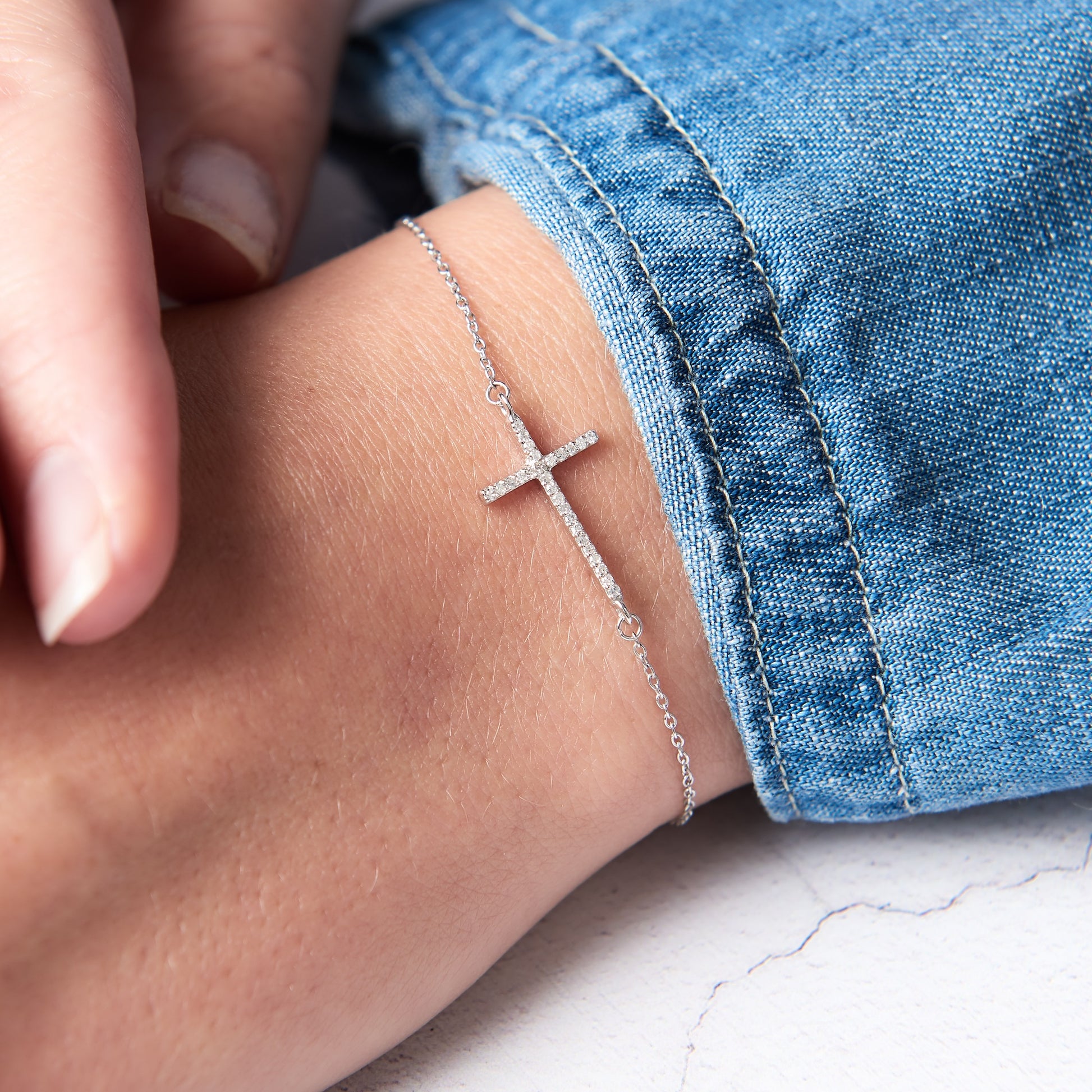 Diamond cross bracelet cast in sterling silver, set with tiny white diamonds on a fine trace chain.  The cross is simple and contemporary and runs sideways across the wrist.