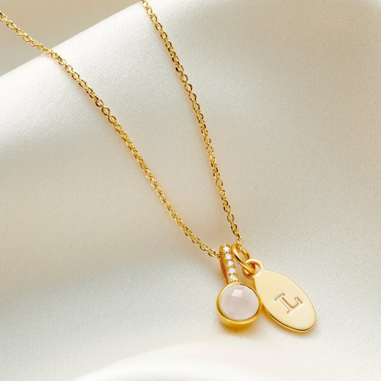 Faceted Rock Crystal Birthstone pendant necklace with little diamonds in the bale with an oval charm personalised with the letter L on a gold trace chain.