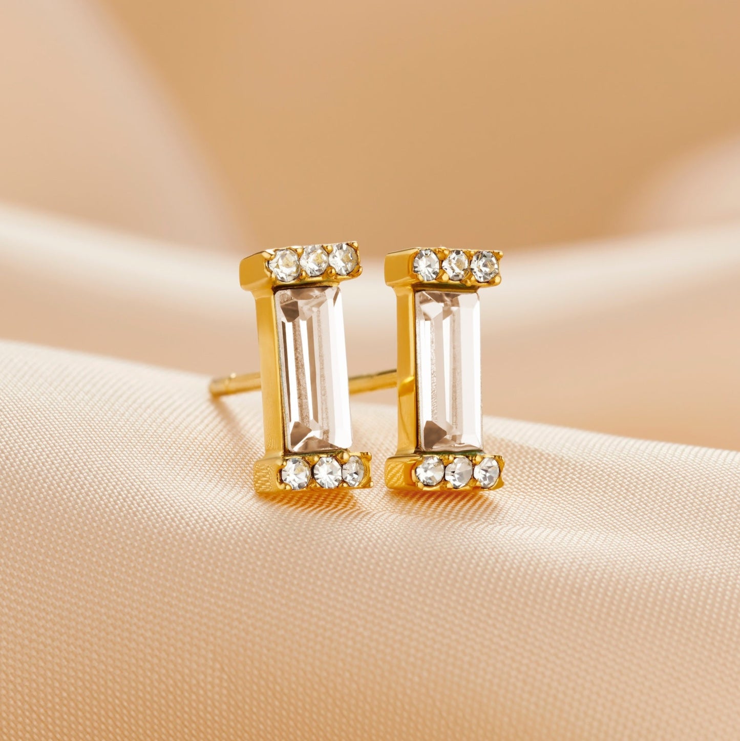 Pair of gold stud earrings set with clear crystal baguette cut stones in a gold setting by Claudette Worters