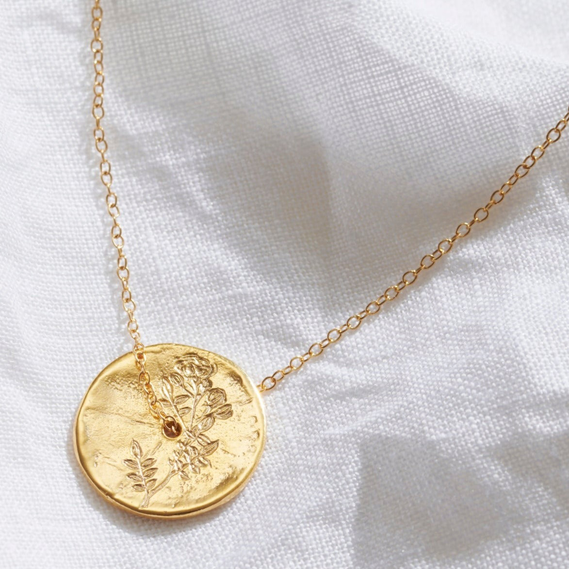 Floral gold coin pendant with hand engraved single Rose stem.  A delicate gold trace chain threads through the centre of the gold disc pendant.