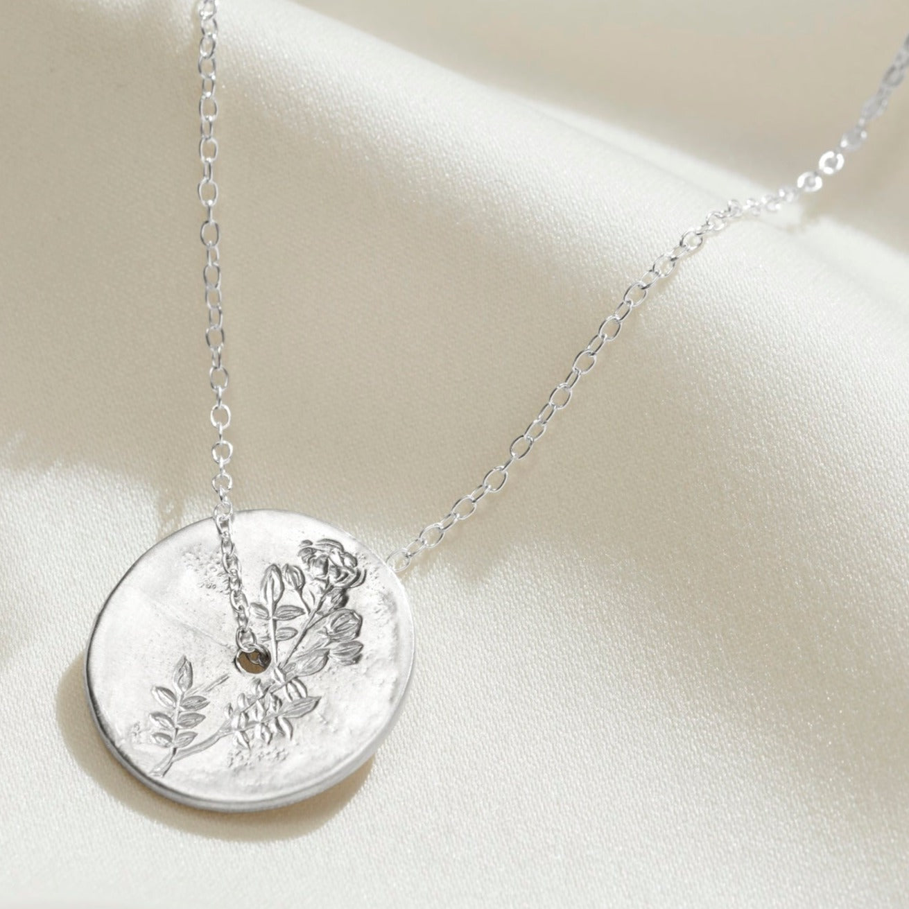 Solid silver disc pendant with a hand engraved rose rose on the surface.  There's a hole in the middle of the pendant with a fine trace chain running through the centre.