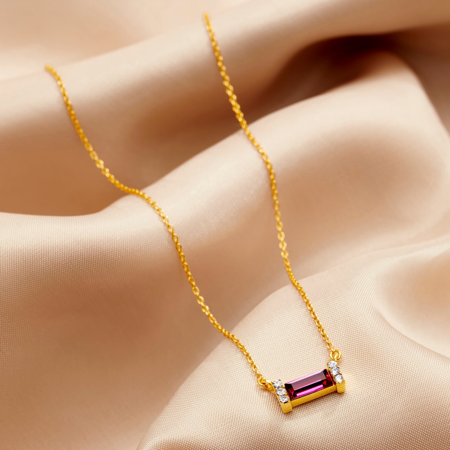 Gold necklace featuring a ruby coloured Swarovski crystal in a baguette shape on a delicate gold trace chain by Claudette Worters.