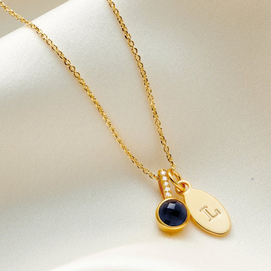 Faceted blue sapphire pendant in 18 carat gold vermeil with little white diamonds in the bale on a fine trace chain with a small oval charm personalised with a capital letter L.