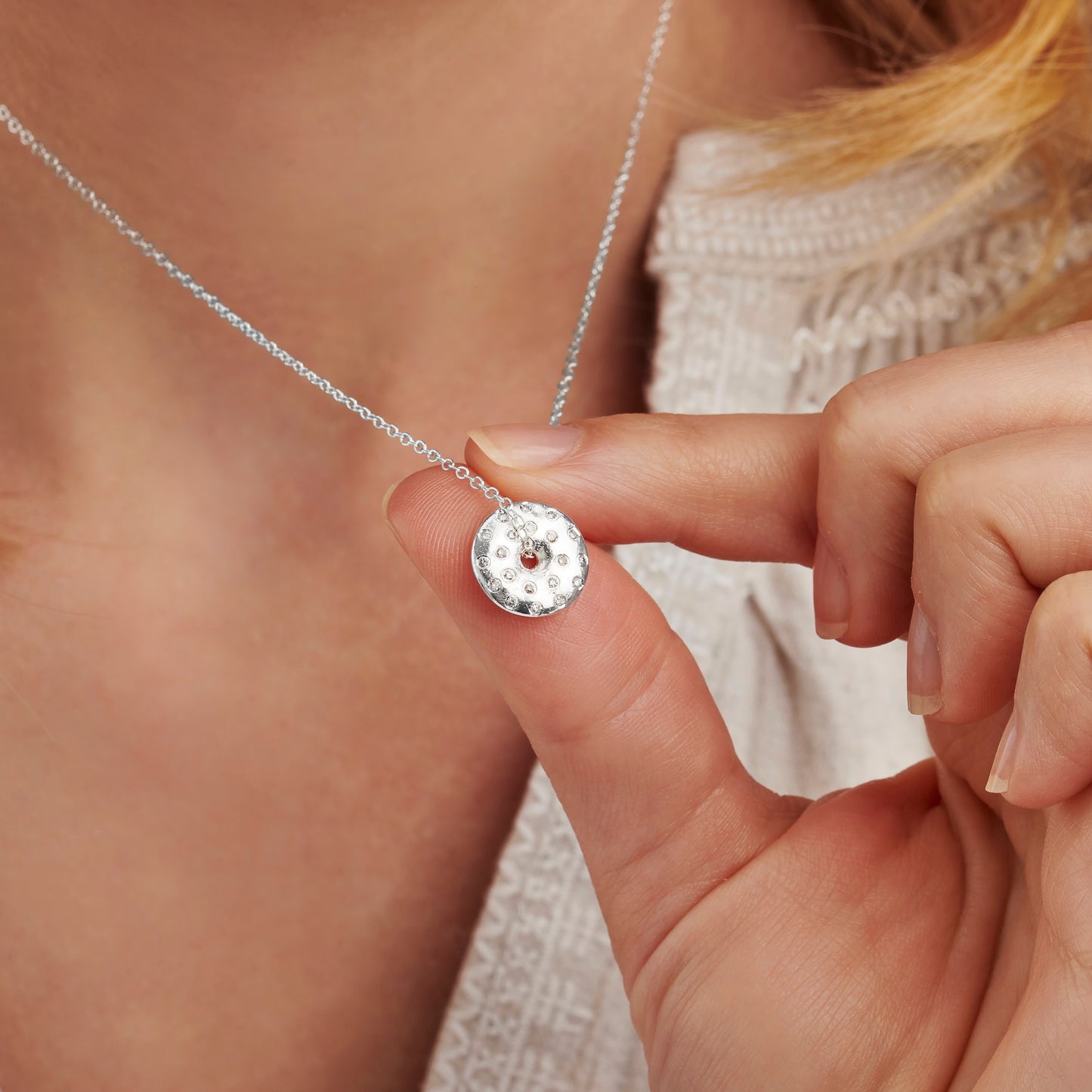 Close-up of a hand holding a silver moon phase necklace with real diamonds on a fine trace chain by Claudette Worters