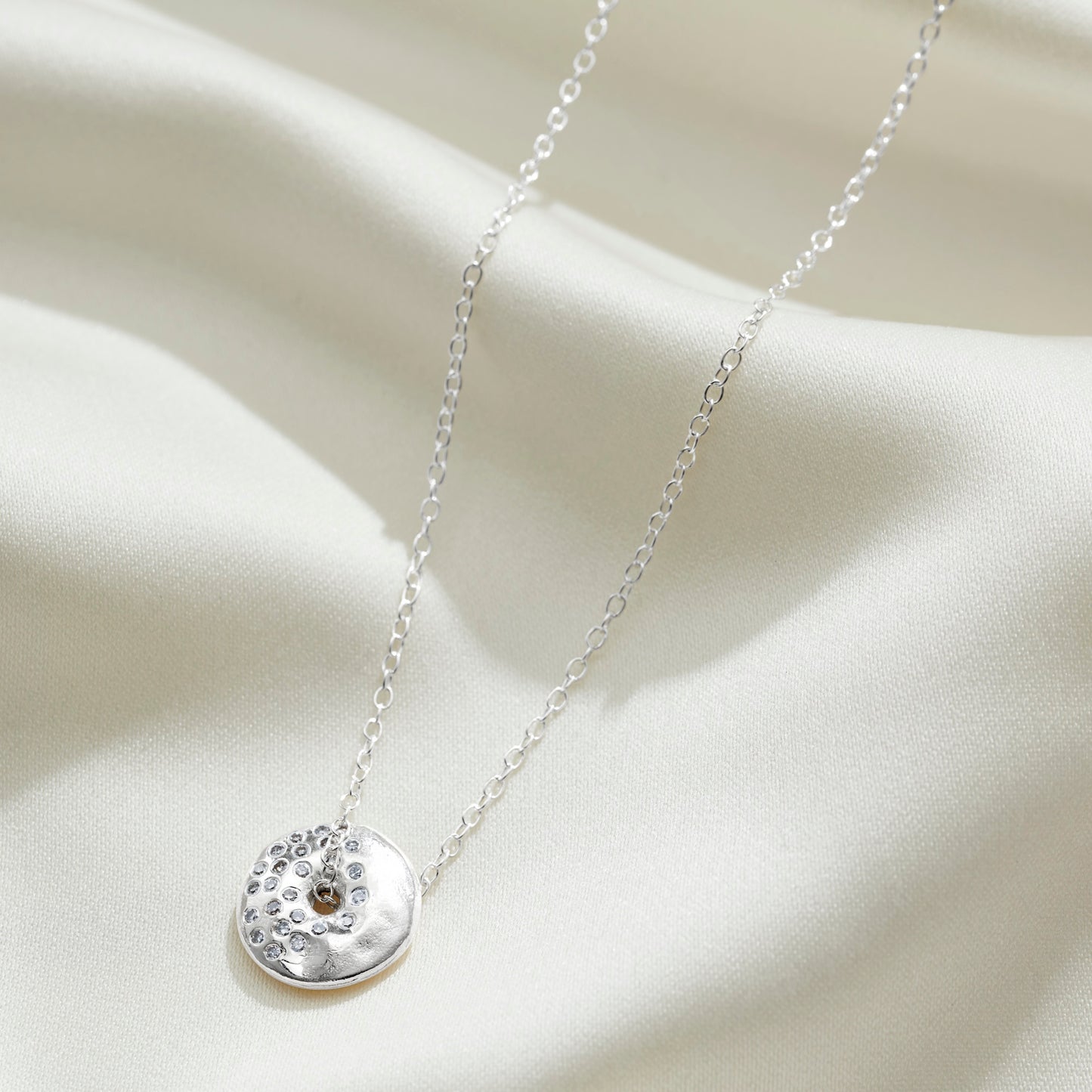 Moon phase necklace in sterling silver, featuring a round silver pendant set with diamonds in the pattern of a waning gibbous moon on a sterling silver trace chain
