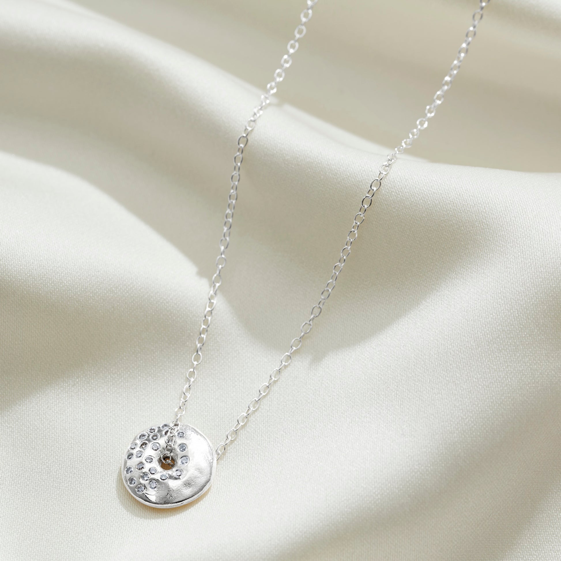 Moon phase necklace in sterling silver, featuring a round silver pendant set with diamonds in the pattern of a waning gibbous moon on a sterling silver trace chain