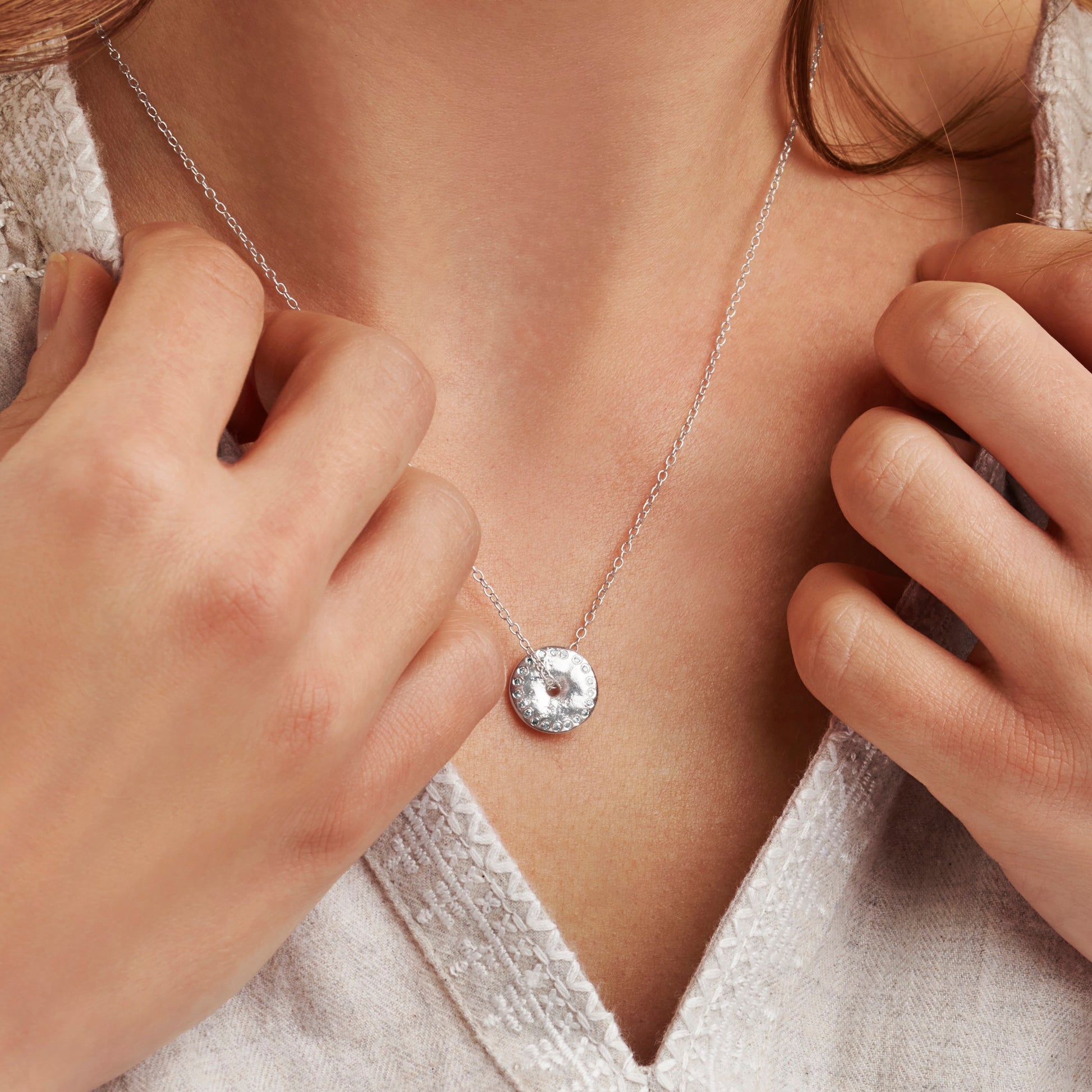 Woman wearing a silver necklace with a round moon phase pendant set with diamonds on a fine silver chain by Claudette Worters