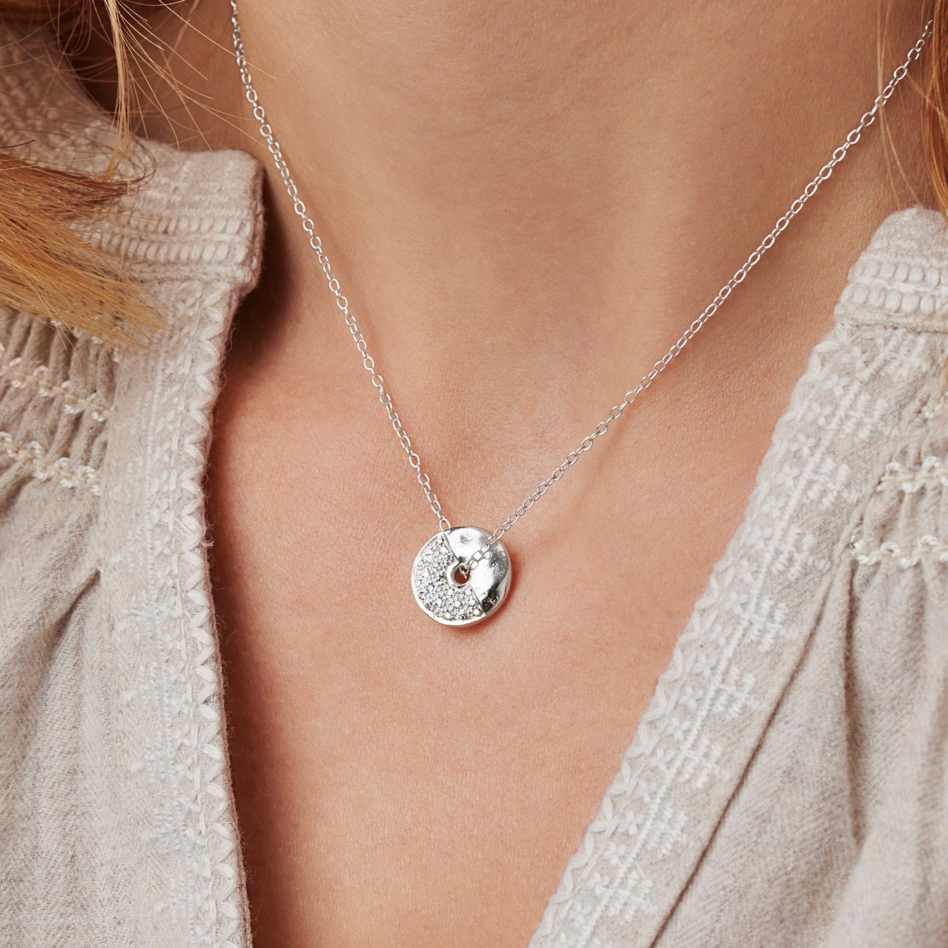 Female model wearing silver moon phase necklace with a disc shaped pendant set with white diamonds with a hole in the middle on a fine sterling silver chain by Claudette Worters