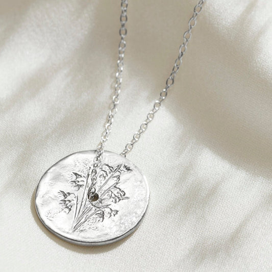 Silver disc necklace with hand engraved snowdrops.  A dainty silver trace chain runs through a hole in the centre of the pendant.