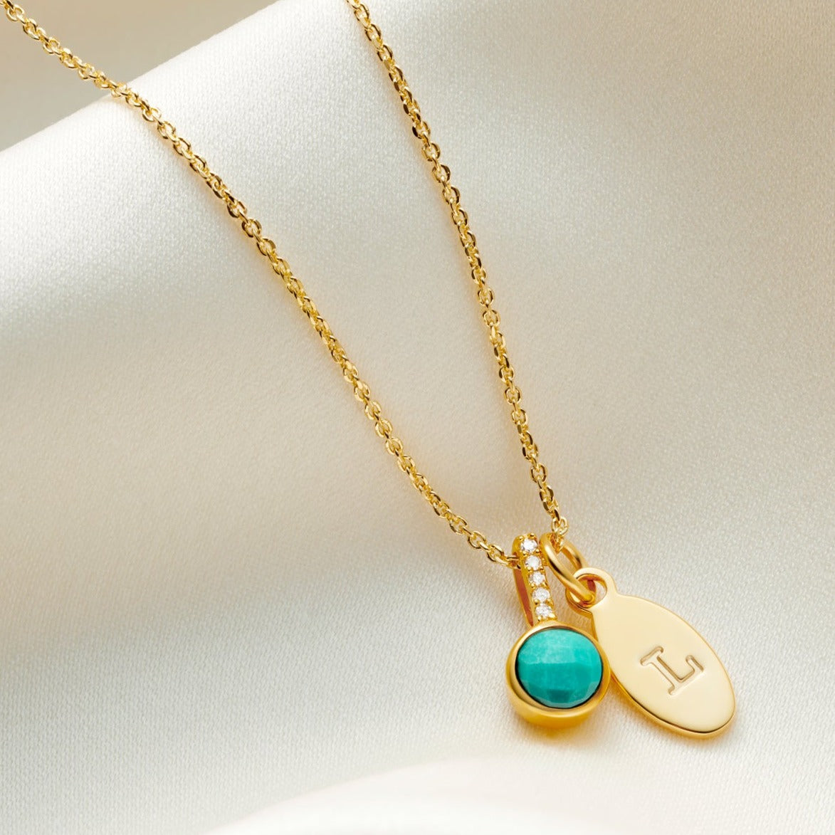 Faceted round turquoise birthstone pendant with tiny white diamonds in the bale on a fine 18 carat gold trace chain with a small oval charm hand stamped with a capital letter L. 