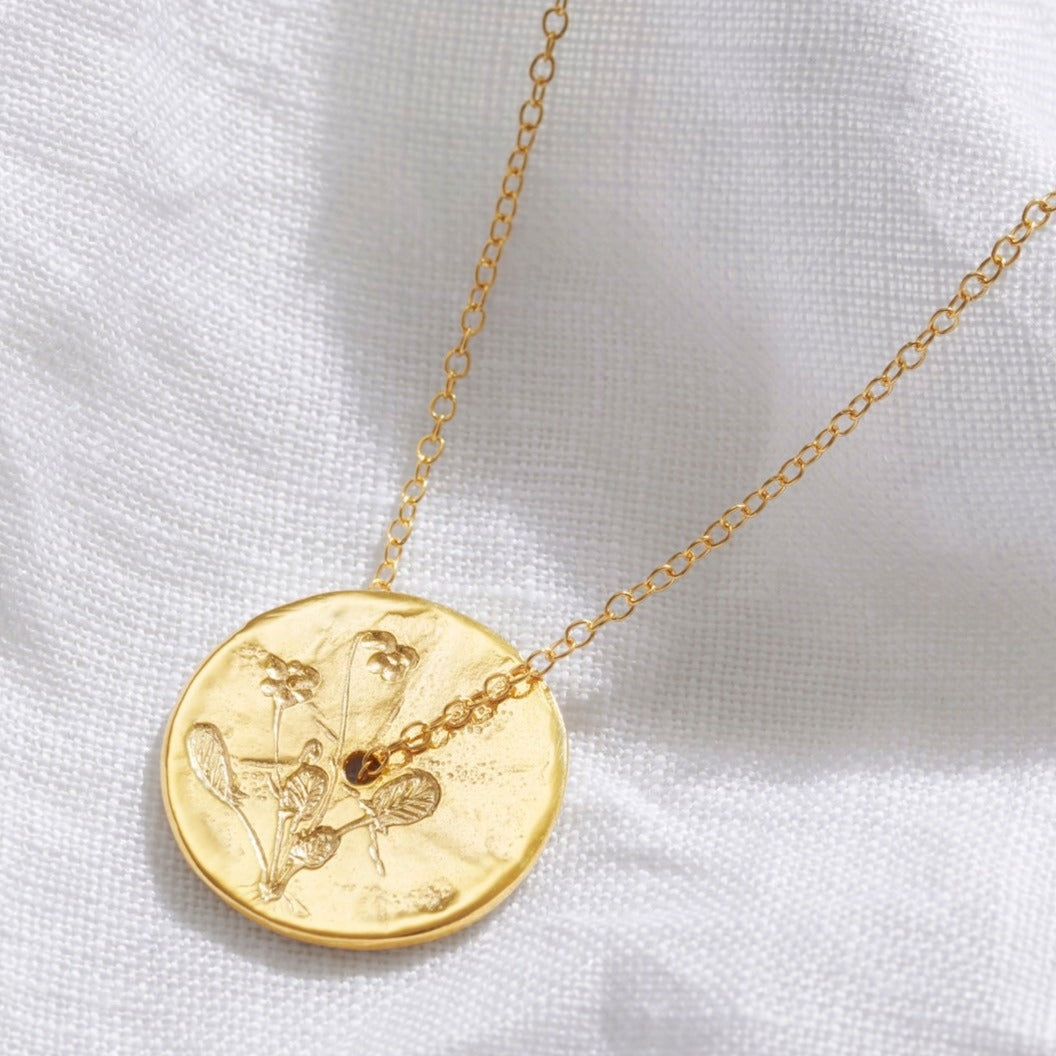 Gold disc pendant with Violet flowers hand engraved on the surface.  There's a hole in the middle of the pendant and a delicate gold trace chain runs through the centre of the birth flower pendant.