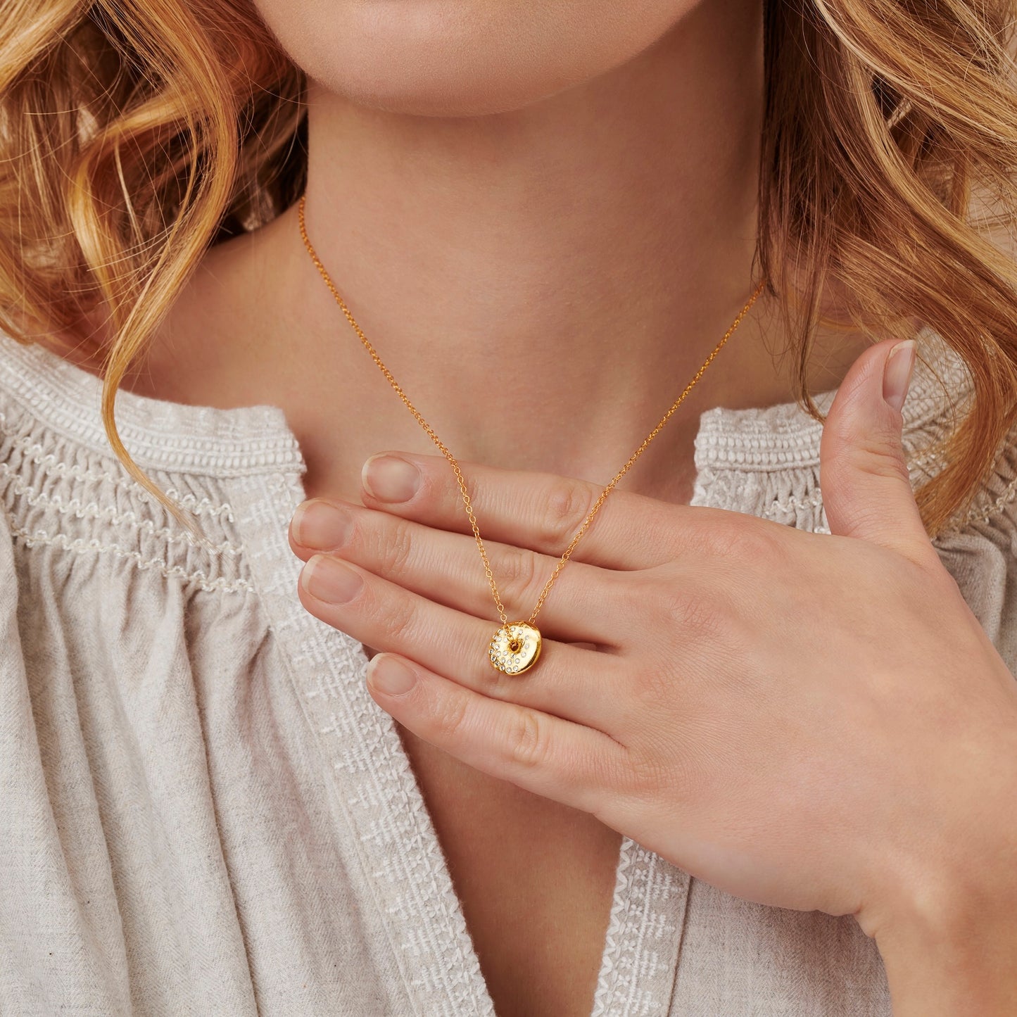 Female model wearing a gold moon phase necklace featuring a dainty polished disc pendant set with white diamonds in the design of the waning gibbous moon phase by Claudette Worters
